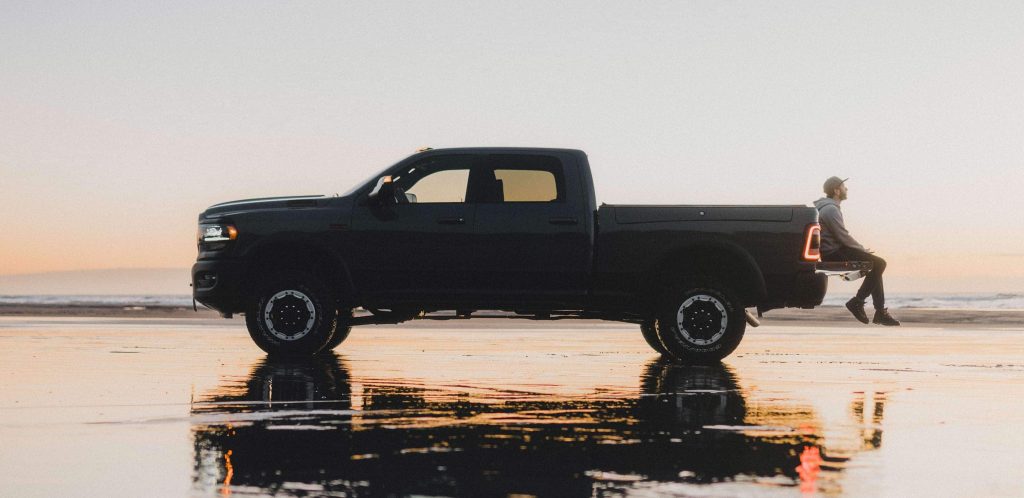 A Ram 2500 truck photographed at dawn. A person is sitting on the open truck bed gate. Only the body shape of the truck is visible against the morning sun.